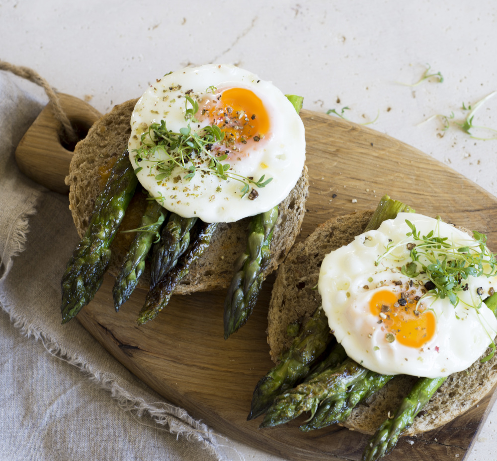 Asparagus and fried egg sandwiches on a wooden board.