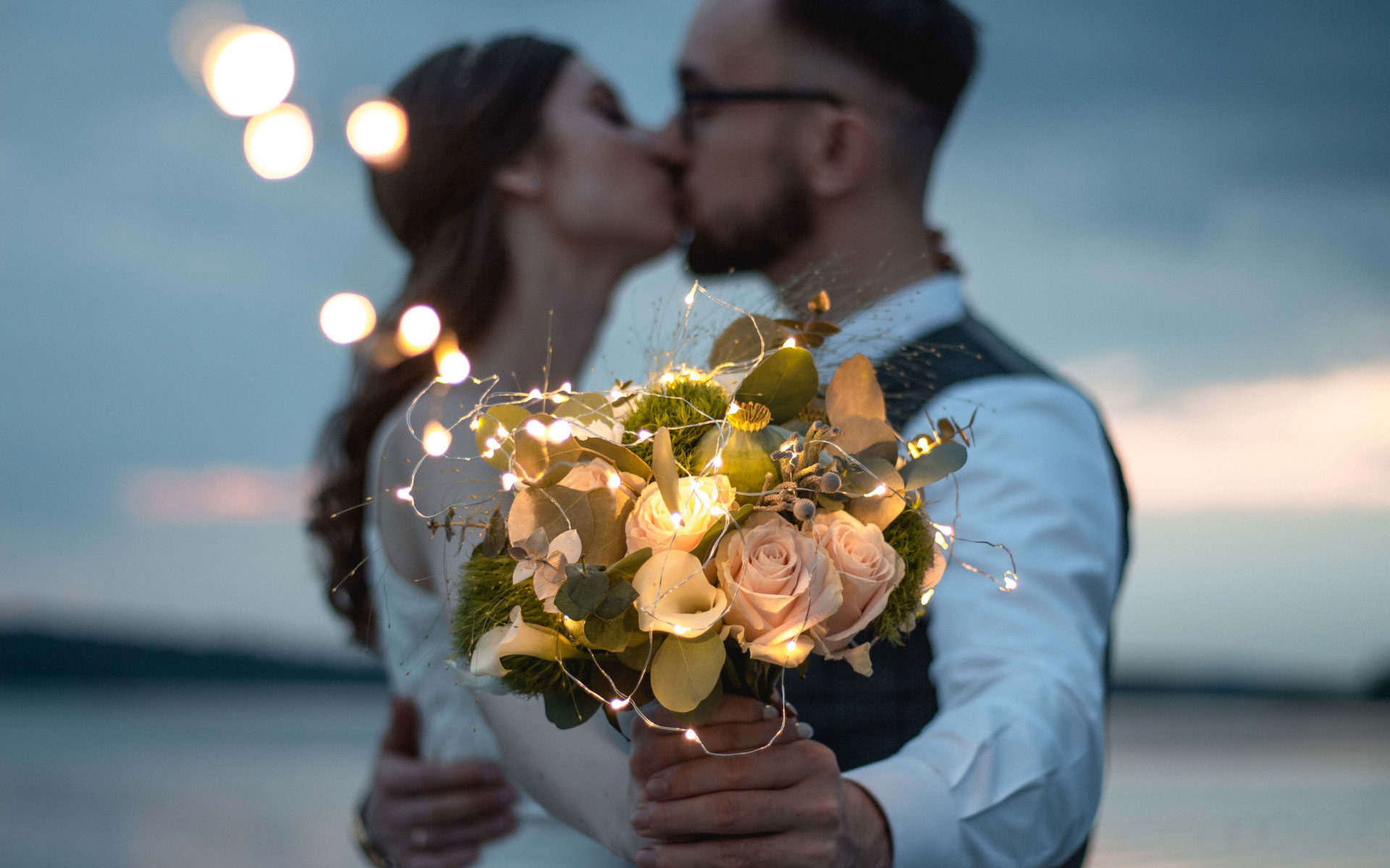 Couple kissing behind a bouquet of flowers with fairy lights.