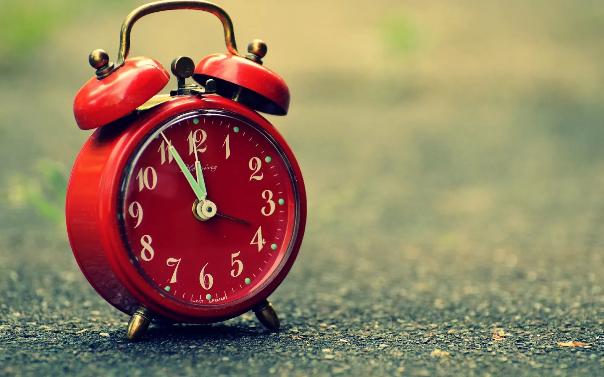Red vintage alarm clock showing almost 12 o'clock.